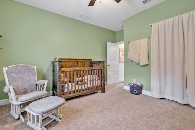 carpeted bedroom with baseboards, a ceiling fan, a crib, and visible vents