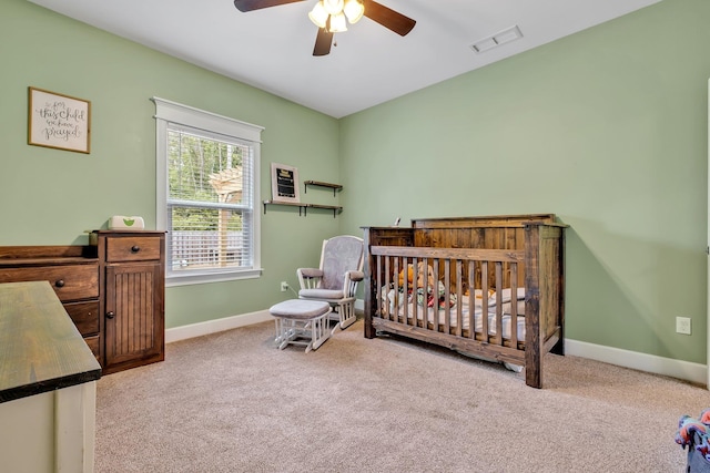 carpeted bedroom featuring baseboards, a ceiling fan, a nursery area, and visible vents