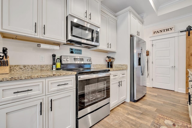 kitchen with a barn door, light wood-style floors, stainless steel appliances, white cabinetry, and ornamental molding