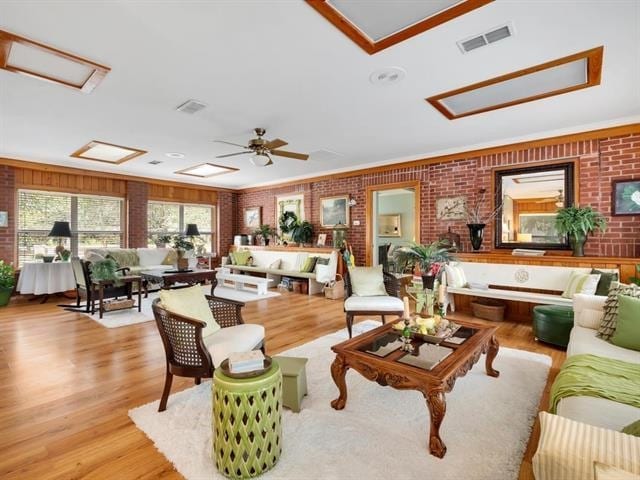 living room with ceiling fan, brick wall, light hardwood / wood-style flooring, and ornamental molding