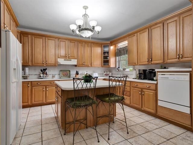 kitchen featuring a kitchen bar, decorative light fixtures, white appliances, a kitchen island, and a notable chandelier