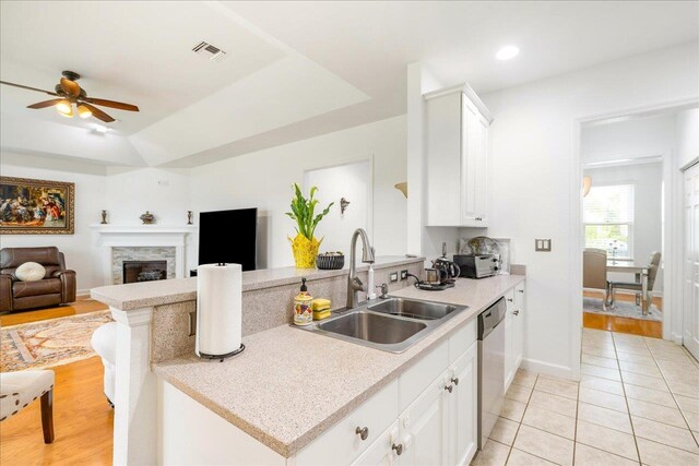 kitchen featuring a stone fireplace, sink, white cabinets, and stainless steel dishwasher