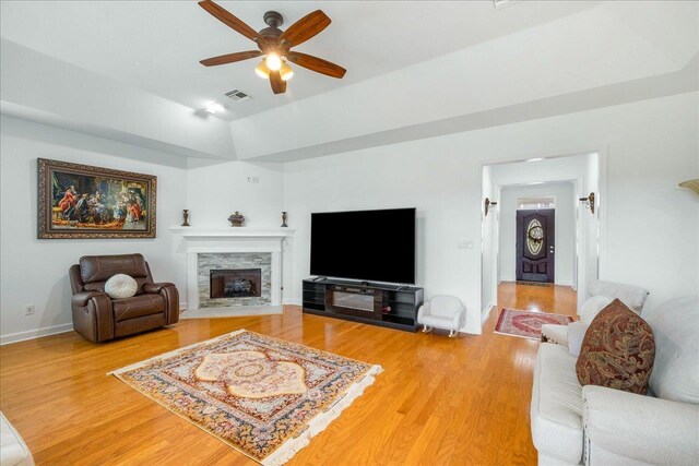 living room with hardwood / wood-style flooring, ceiling fan, and a stone fireplace