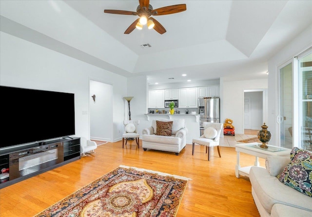 living room featuring a tray ceiling, ceiling fan, and light hardwood / wood-style flooring