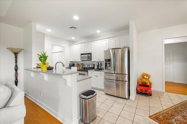 kitchen with kitchen peninsula, a breakfast bar, stainless steel appliances, light tile patterned floors, and white cabinetry