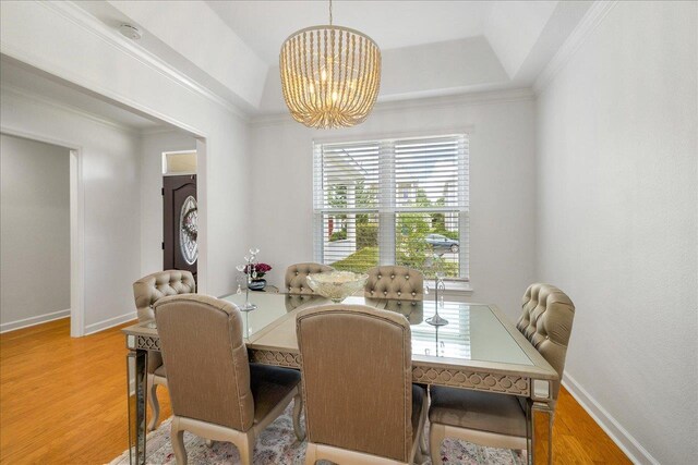 dining space with a raised ceiling, wood-type flooring, crown molding, and an inviting chandelier