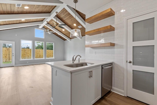 kitchen featuring a sink, lofted ceiling with beams, stainless steel dishwasher, wood finished floors, and light countertops