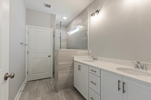 bathroom featuring double vanity, visible vents, a tile shower, and a sink