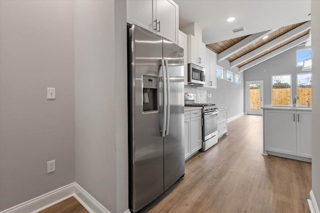 kitchen featuring visible vents, baseboards, vaulted ceiling with beams, light wood-style floors, and appliances with stainless steel finishes