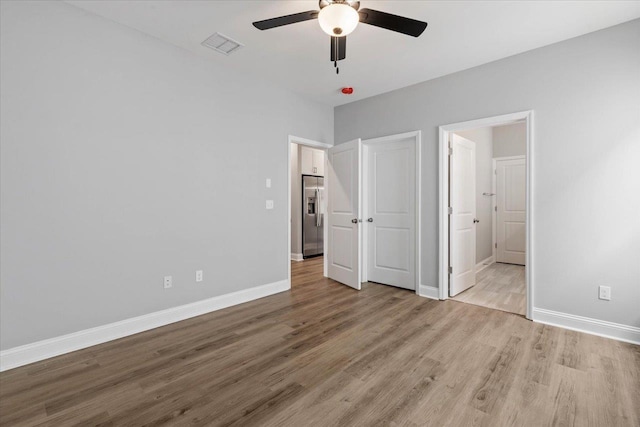 unfurnished bedroom with visible vents, light wood-type flooring, baseboards, and stainless steel fridge with ice dispenser