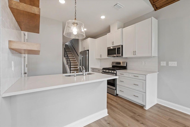 kitchen with visible vents, a peninsula, light wood-style floors, stainless steel appliances, and a sink