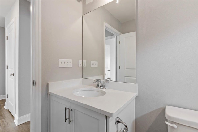 half bathroom featuring baseboards, toilet, wood finished floors, and vanity