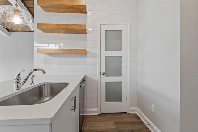 kitchen featuring a sink, open shelves, light countertops, stainless steel dishwasher, and dark wood-style flooring