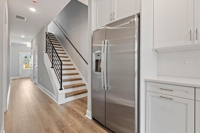 kitchen featuring light wood finished floors, stainless steel refrigerator with ice dispenser, tasteful backsplash, white cabinets, and light countertops