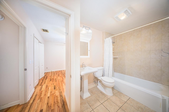 bathroom featuring toilet, shower / bathtub combination with curtain, visible vents, and tile patterned floors