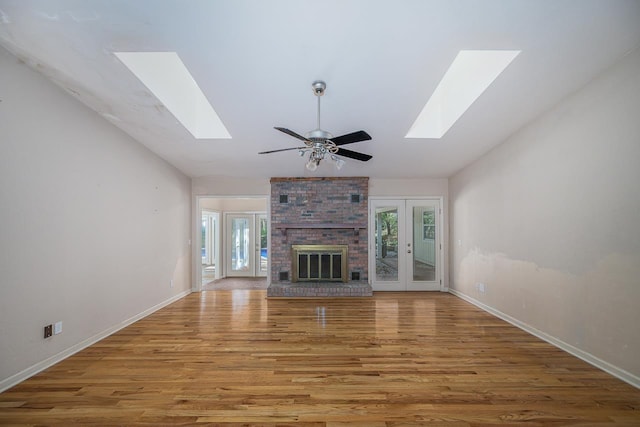 unfurnished living room with lofted ceiling with skylight, a brick fireplace, wood finished floors, and a healthy amount of sunlight