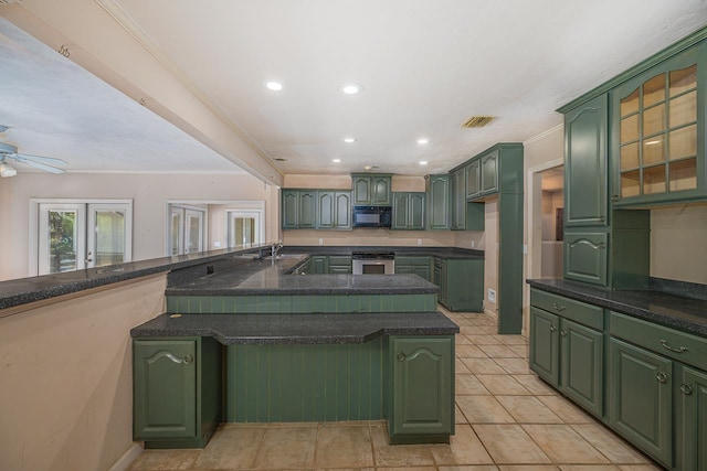 kitchen featuring black microwave, green cabinetry, oven, and visible vents