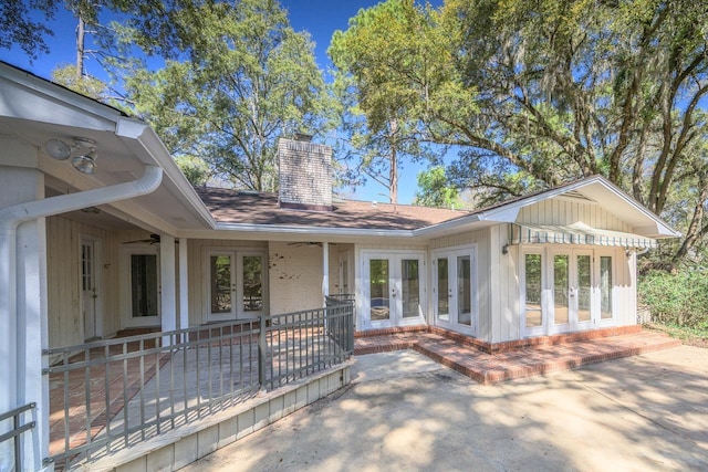 view of front facade featuring french doors, brick siding, a patio, a chimney, and a shingled roof