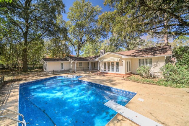 rear view of property with fence, french doors, a fenced in pool, a chimney, and a patio area