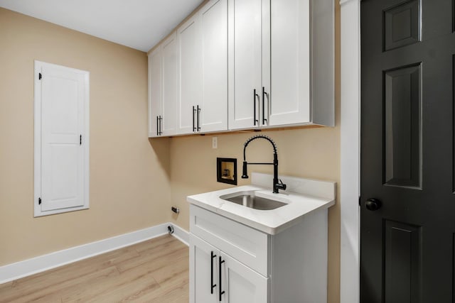 washroom featuring washer hookup, a sink, baseboards, light wood-type flooring, and cabinet space