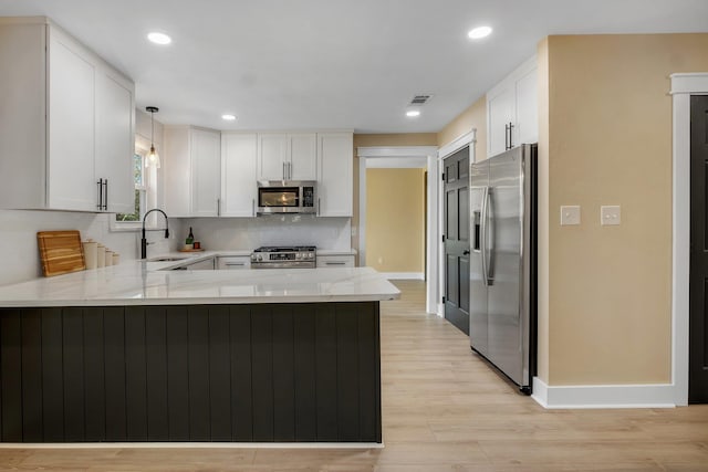 kitchen with a peninsula, a sink, white cabinetry, hanging light fixtures, and appliances with stainless steel finishes