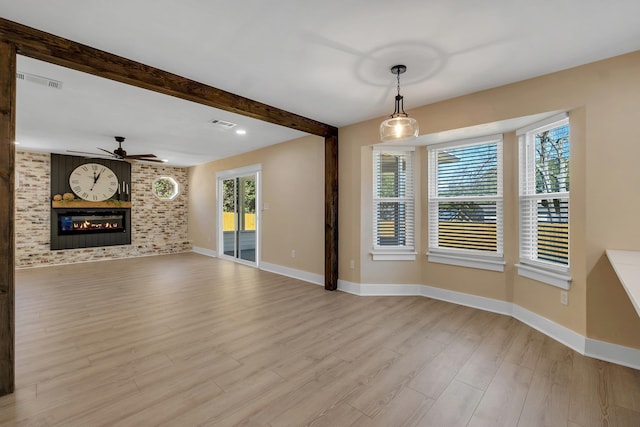 unfurnished living room featuring a large fireplace, baseboards, visible vents, beamed ceiling, and light wood-type flooring