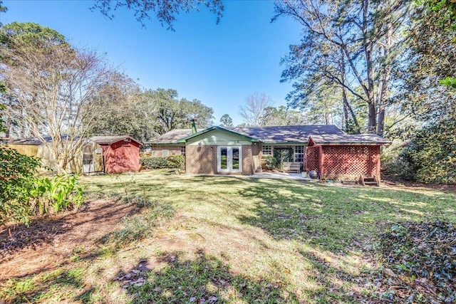 back of house featuring brick siding, an outdoor structure, a yard, french doors, and a shed