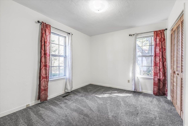 carpeted empty room with a wealth of natural light, visible vents, a textured ceiling, and baseboards