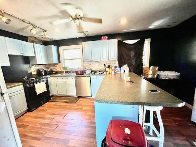 kitchen featuring stainless steel dishwasher, a kitchen breakfast bar, light wood-type flooring, and white cabinetry