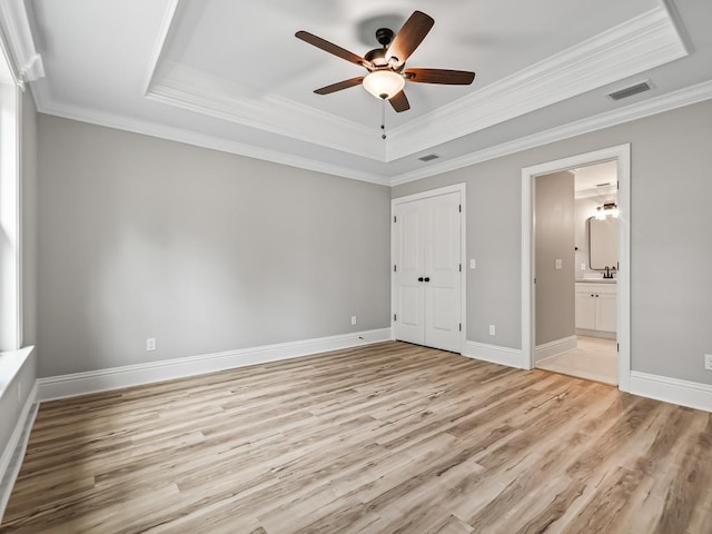 unfurnished bedroom featuring ceiling fan, ensuite bathroom, ornamental molding, a raised ceiling, and a closet