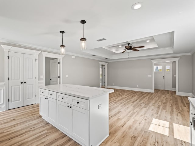 kitchen with ornamental molding, a raised ceiling, a kitchen island, light stone countertops, and white cabinets