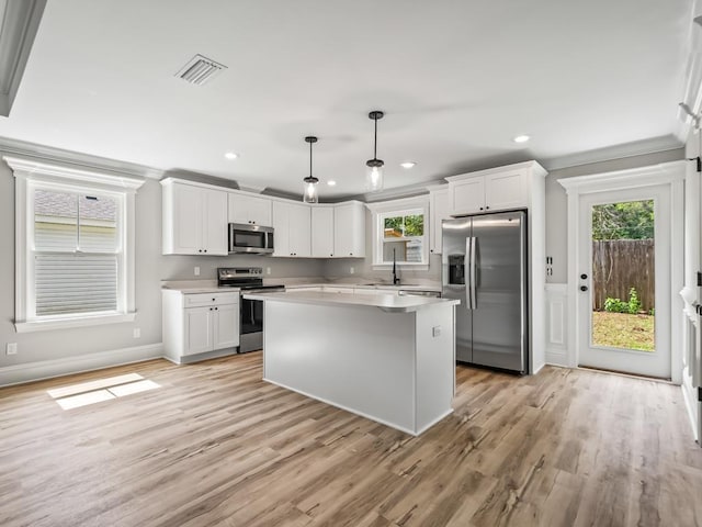 kitchen featuring white cabinetry, crown molding, a center island, hanging light fixtures, and appliances with stainless steel finishes