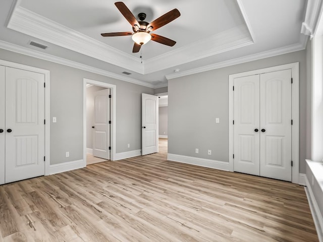 unfurnished bedroom with crown molding, light hardwood / wood-style flooring, ceiling fan, and a tray ceiling