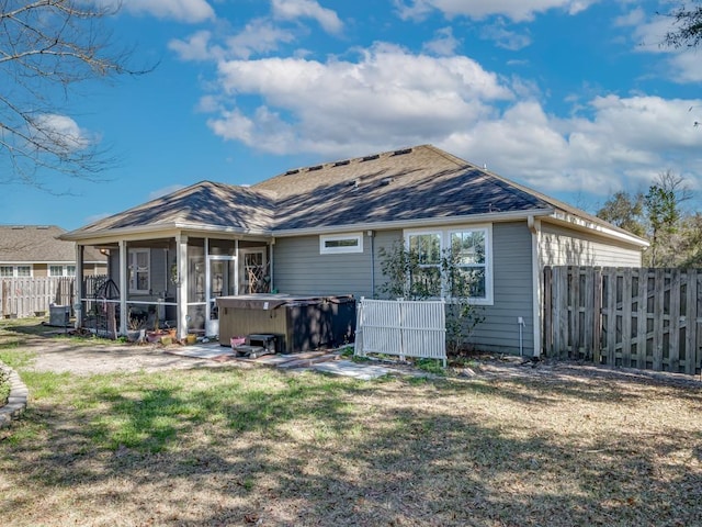 rear view of property featuring a lawn, a sunroom, a patio area, and a hot tub