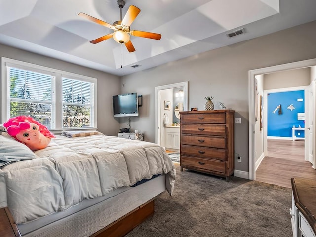 carpeted bedroom with a tray ceiling, connected bathroom, and ceiling fan