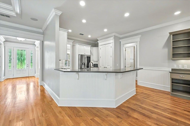 kitchen with stainless steel refrigerator with ice dispenser, a kitchen breakfast bar, light wood-style flooring, dark countertops, and a peninsula