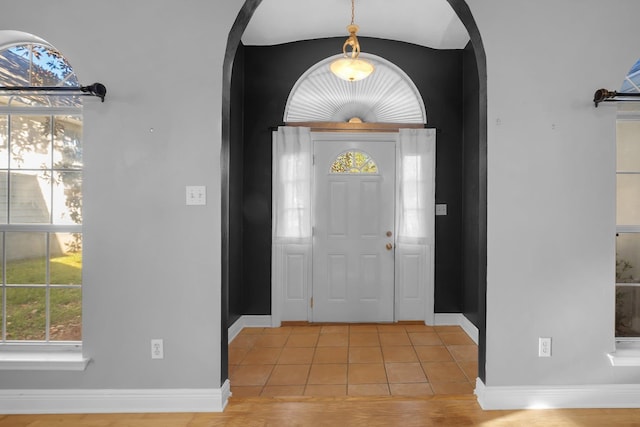 entryway with light tile patterned floors, baseboards, and arched walkways