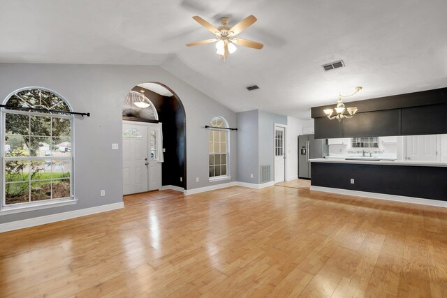 unfurnished living room with light wood-style floors, arched walkways, visible vents, and ceiling fan with notable chandelier