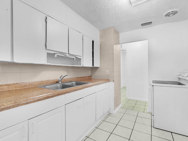 kitchen with sink, light tile patterned floors, washer / clothes dryer, a textured ceiling, and white cabinets