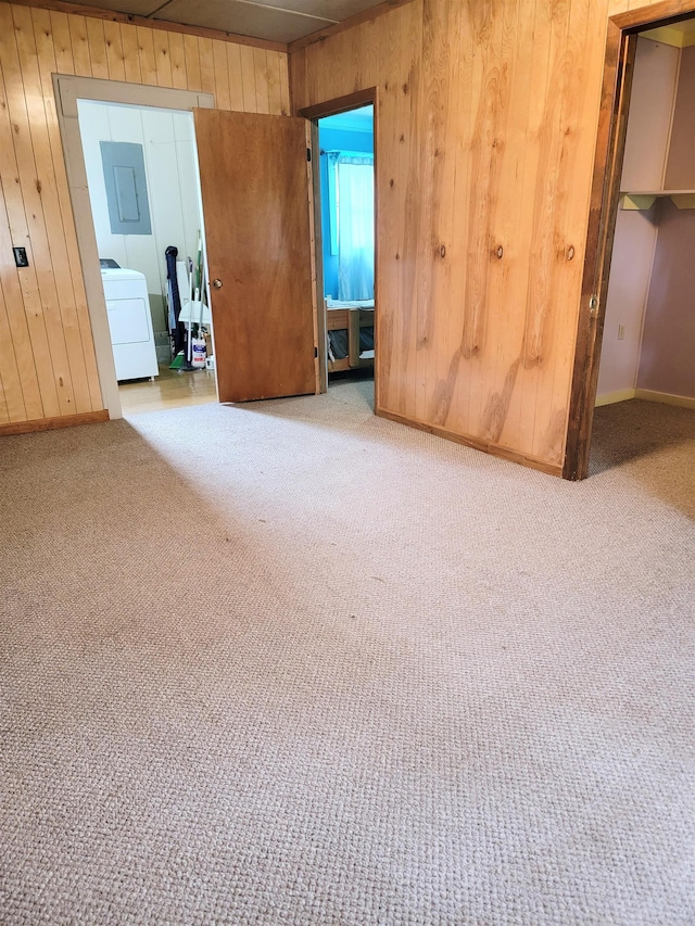 spare room featuring washer / dryer, wood walls, electric panel, and light colored carpet