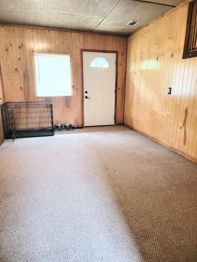 foyer entrance with wooden walls and carpet flooring