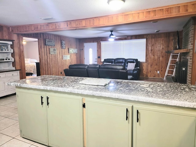 kitchen with light stone counters, ceiling fan, light tile patterned flooring, and wood walls