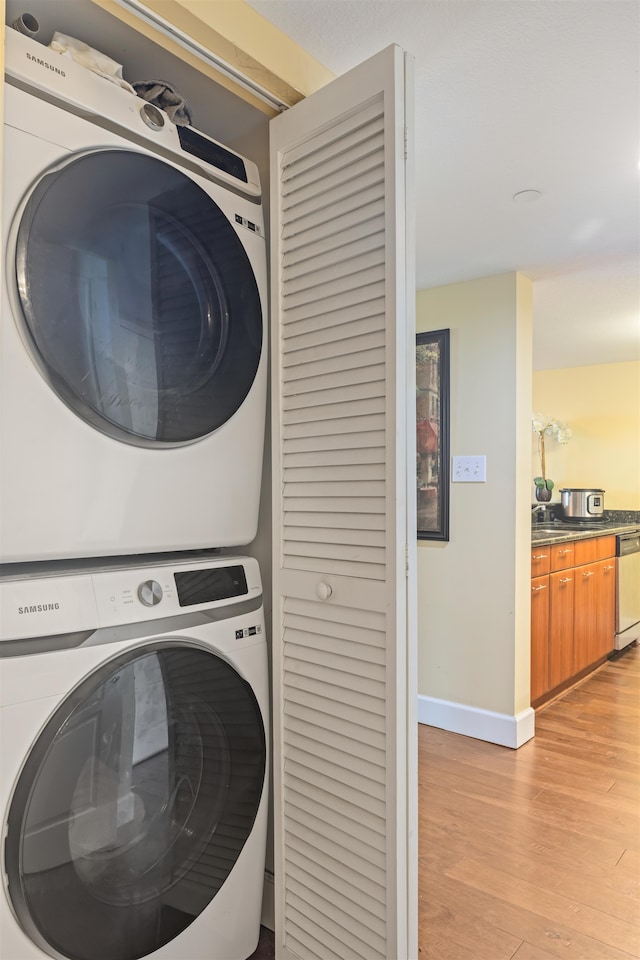 washroom with laundry area, baseboards, light wood finished floors, and stacked washer / dryer