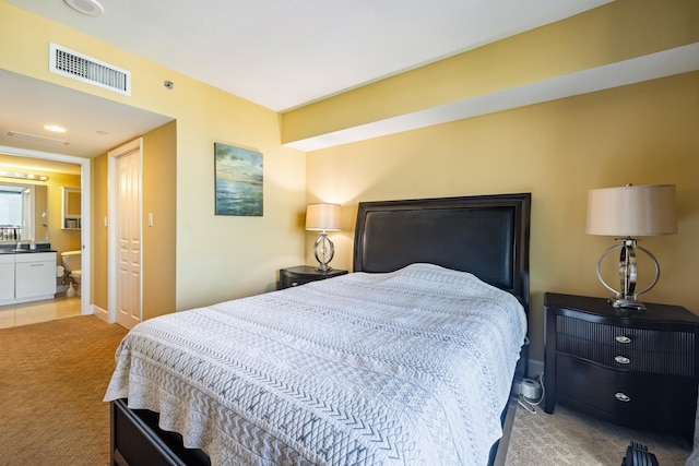 bedroom with light carpet, visible vents, and ensuite bathroom