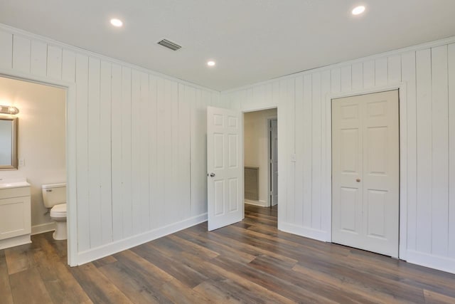 unfurnished bedroom with dark hardwood / wood-style flooring, a closet, wooden walls, and ensuite bathroom