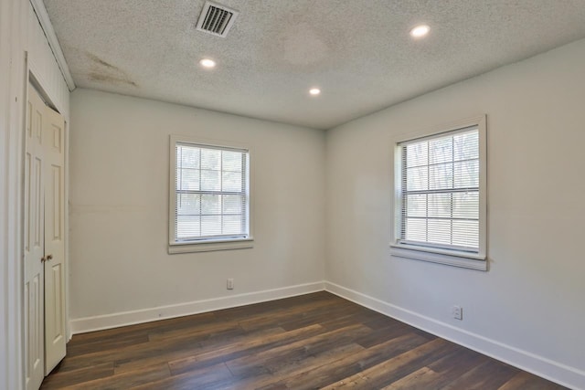 spare room with a wealth of natural light, a textured ceiling, and dark hardwood / wood-style floors