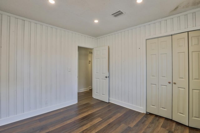 unfurnished bedroom featuring ornamental molding, a textured ceiling, wooden walls, a closet, and dark hardwood / wood-style flooring