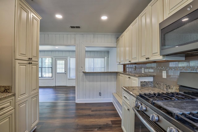 kitchen with stainless steel appliances, tasteful backsplash, dark stone countertops, and dark hardwood / wood-style flooring