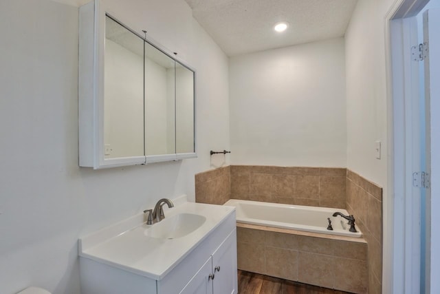 bathroom featuring hardwood / wood-style floors, vanity, a textured ceiling, and tiled tub