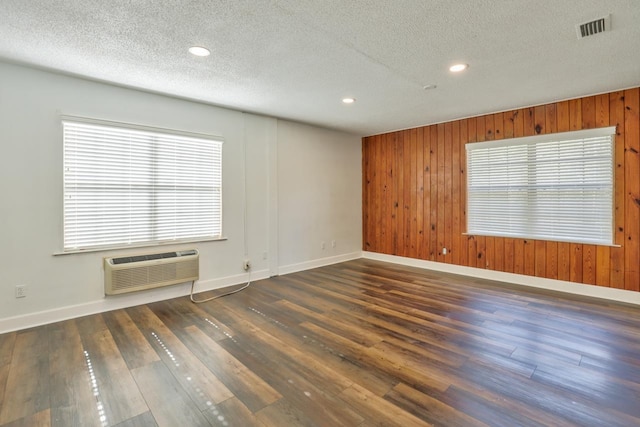 unfurnished room with an AC wall unit, wood walls, a textured ceiling, and dark hardwood / wood-style floors